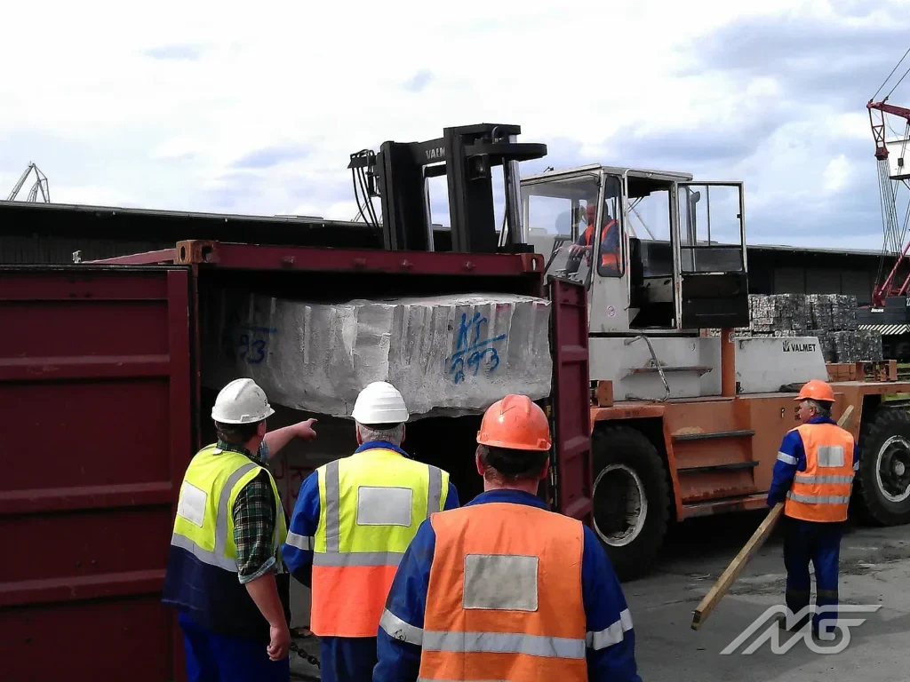 Stevedoring gang and a forklift truck removing a stone block from a container at the quayside